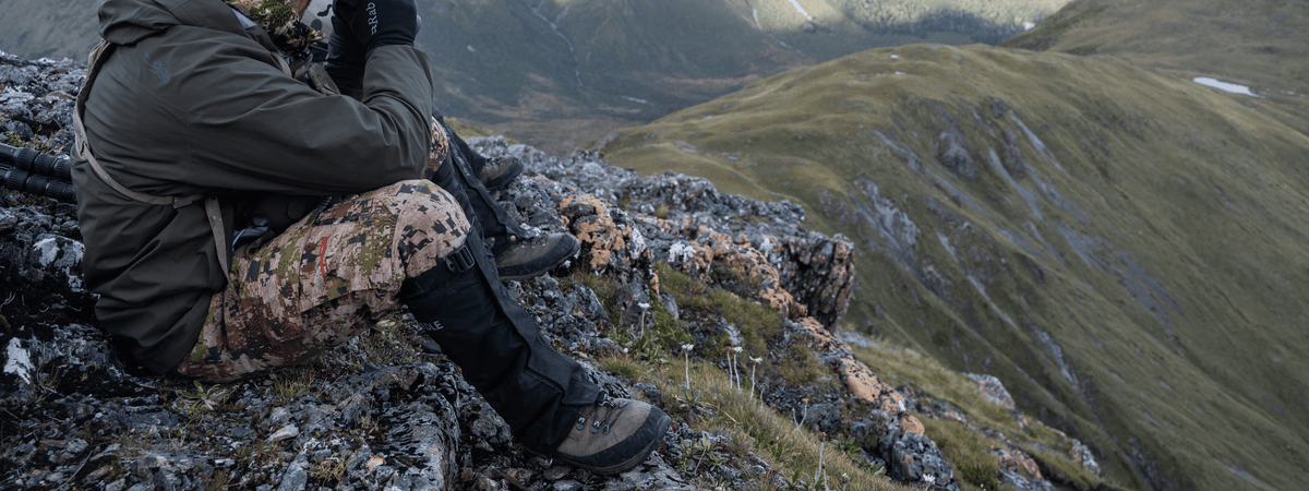 man sittiing on mountain top with lowa hiking boots and gaiters