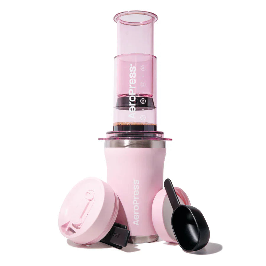 Pink AeroPress coffee maker with components on a white background