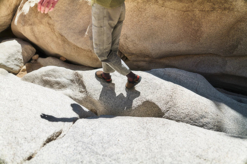 Person wearing the bedrock sandals mountain clogs in synthetic suede pinecone walking on a boulder