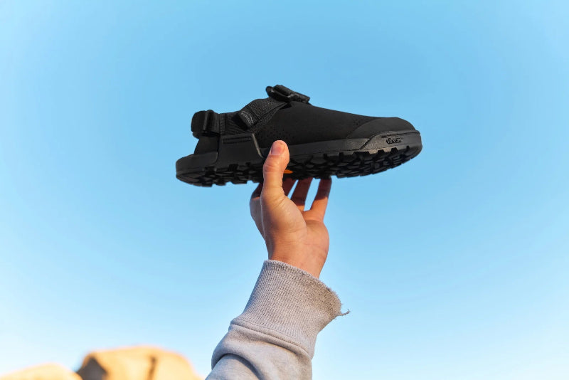 Person holding a black shoe against a clear blue sky