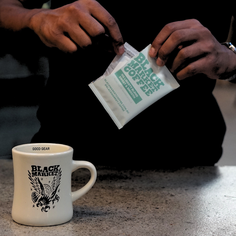 A Black Market Coffee cup on a table and a person tearing open the packaing