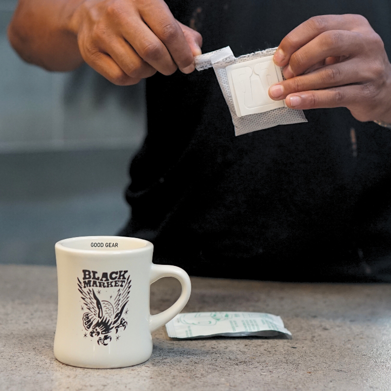 A black market coffee filter being opened with a coffee mug on a table