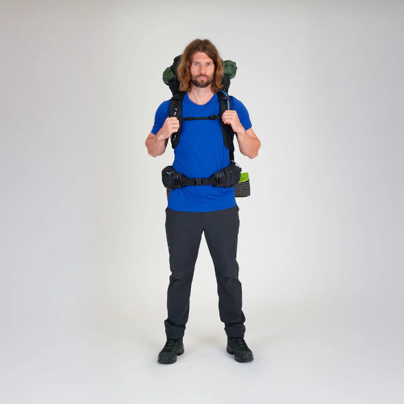 Man wearing a blue shirt and black pants with a large backpack on a white background