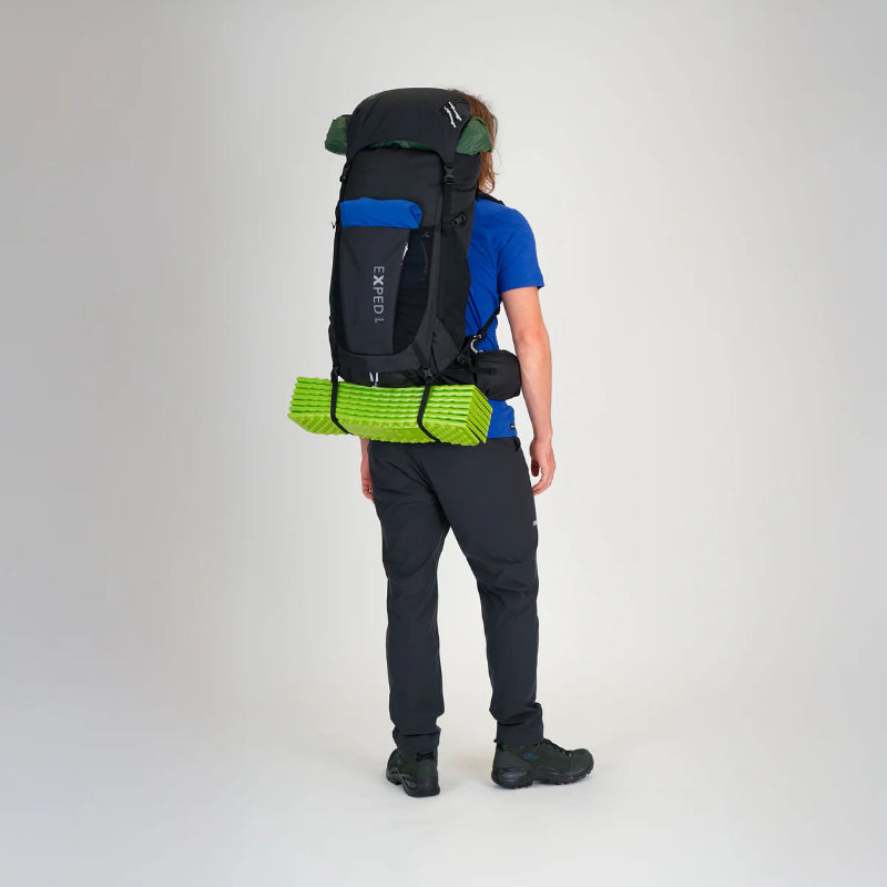 Person wearing a large black backpack with green accents on a plain background