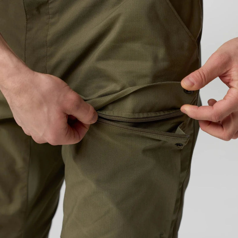 Person adjusting a pocket on a green jacket against a neutral background