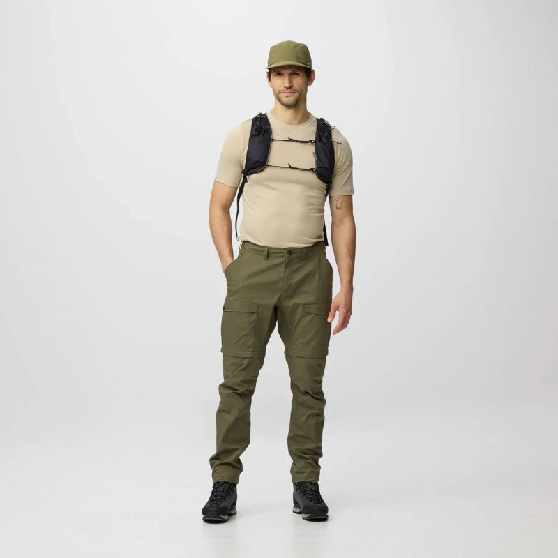 Man wearing a beige shirt, green pants, and a cap with a black backpack on a white background