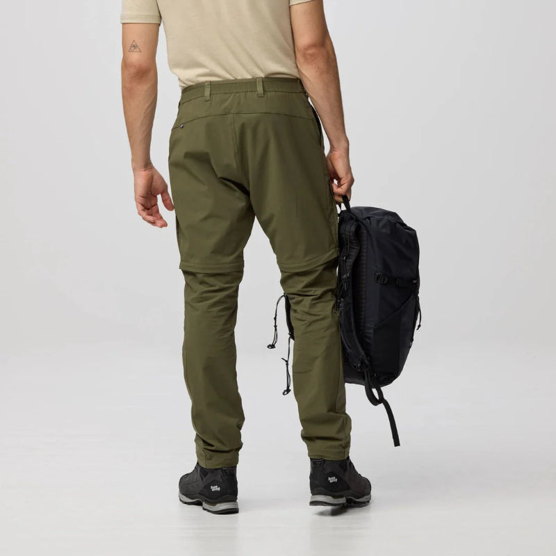 Person wearing green pants and black shoes with a black backpack on a white background