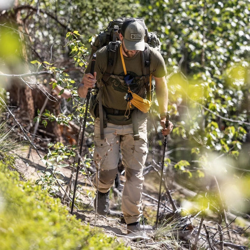 Hiker with a backpack and walking sticks navigating a forest trail