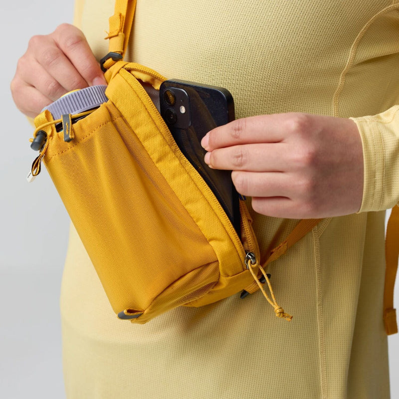 Person holding a yellow waist bag with a phone in it against a light gray background