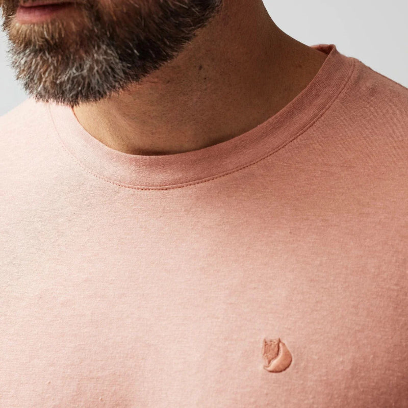 Close-up of a person wearing a pink t-shirt with a small logo on a light gray background