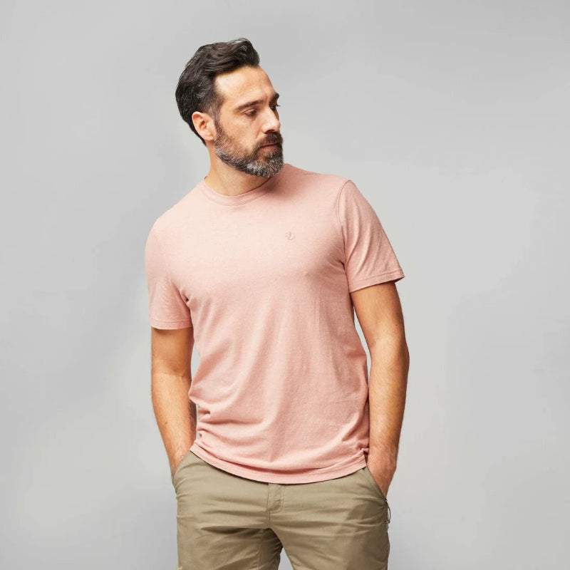 Man wearing a pink t-shirt and beige pants against a gray background