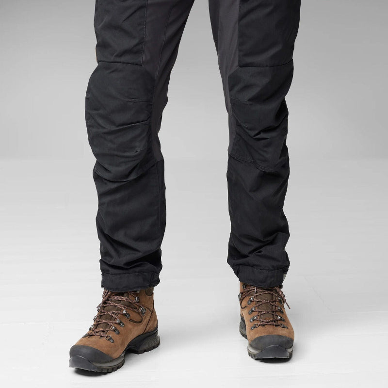 Black pants worn with brown hiking boots on a light gray background