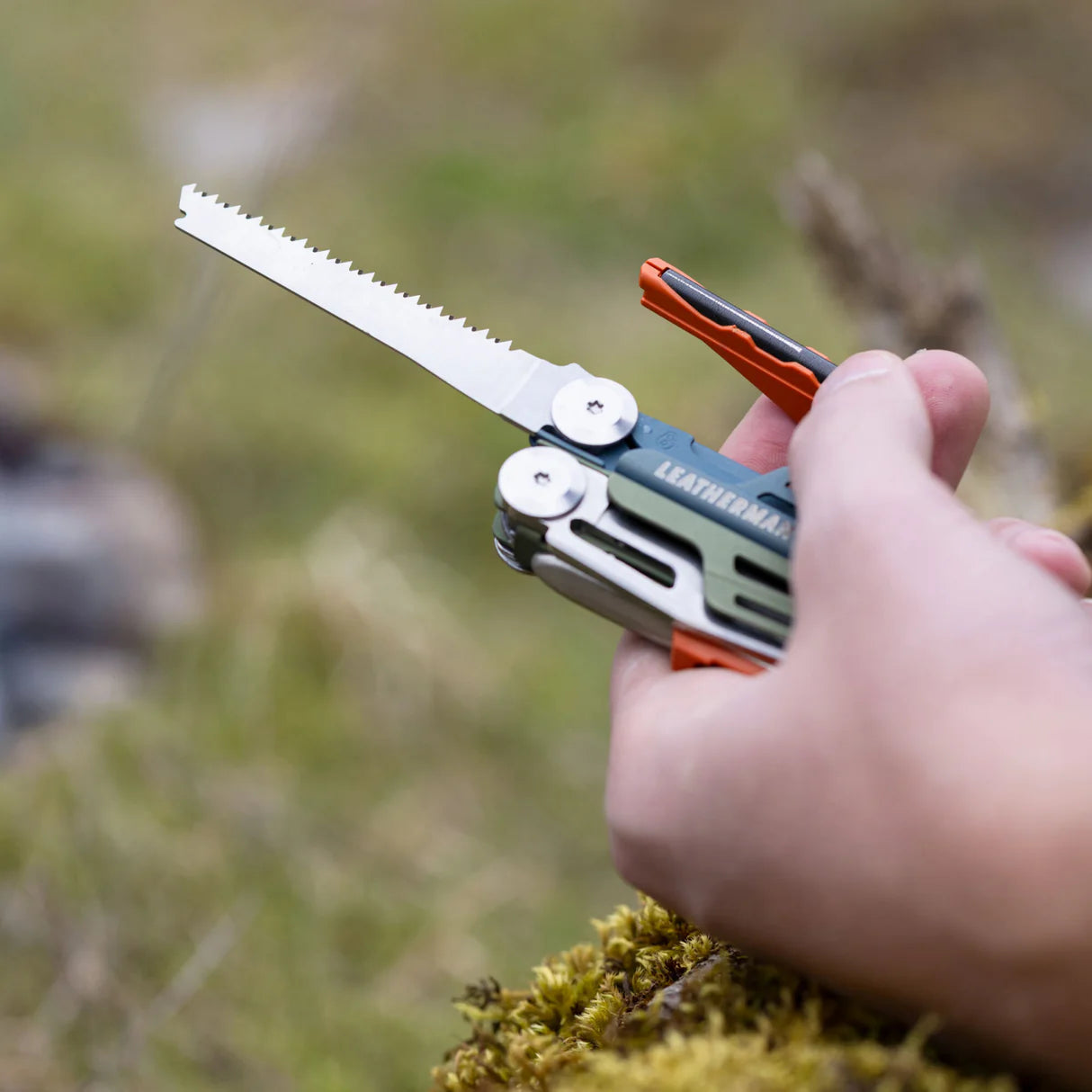 Multitool with saw attachment held by a hand against a natural background
