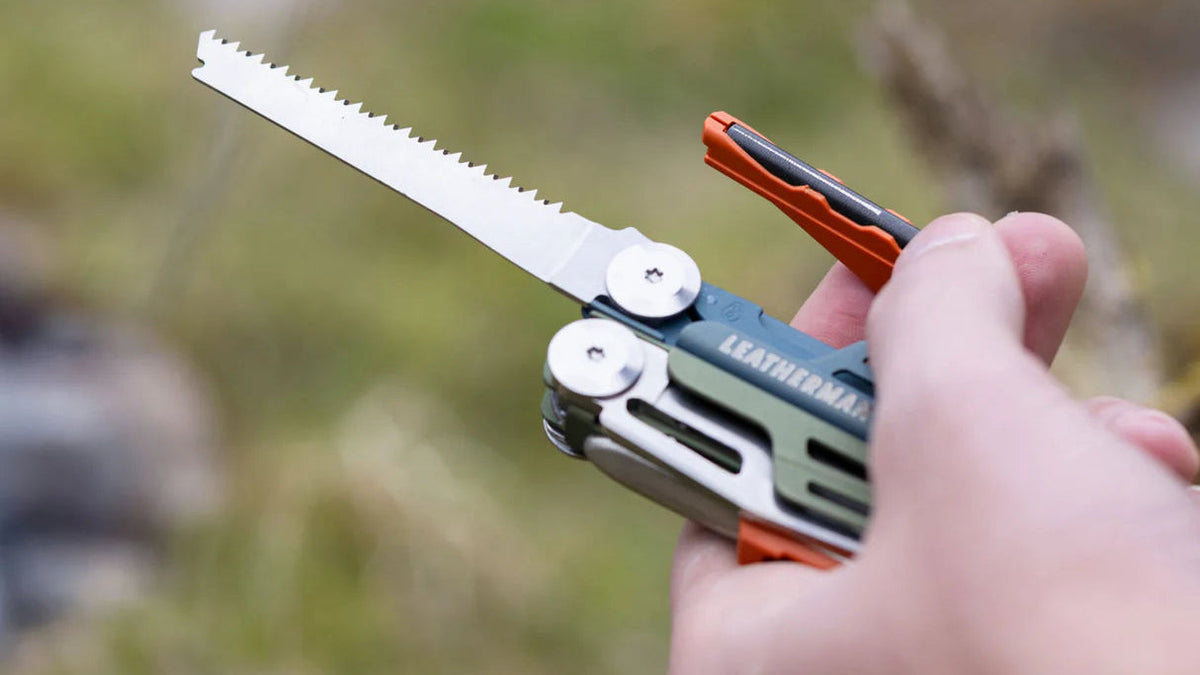 Multitool with saw attachment held by a hand against a natural background