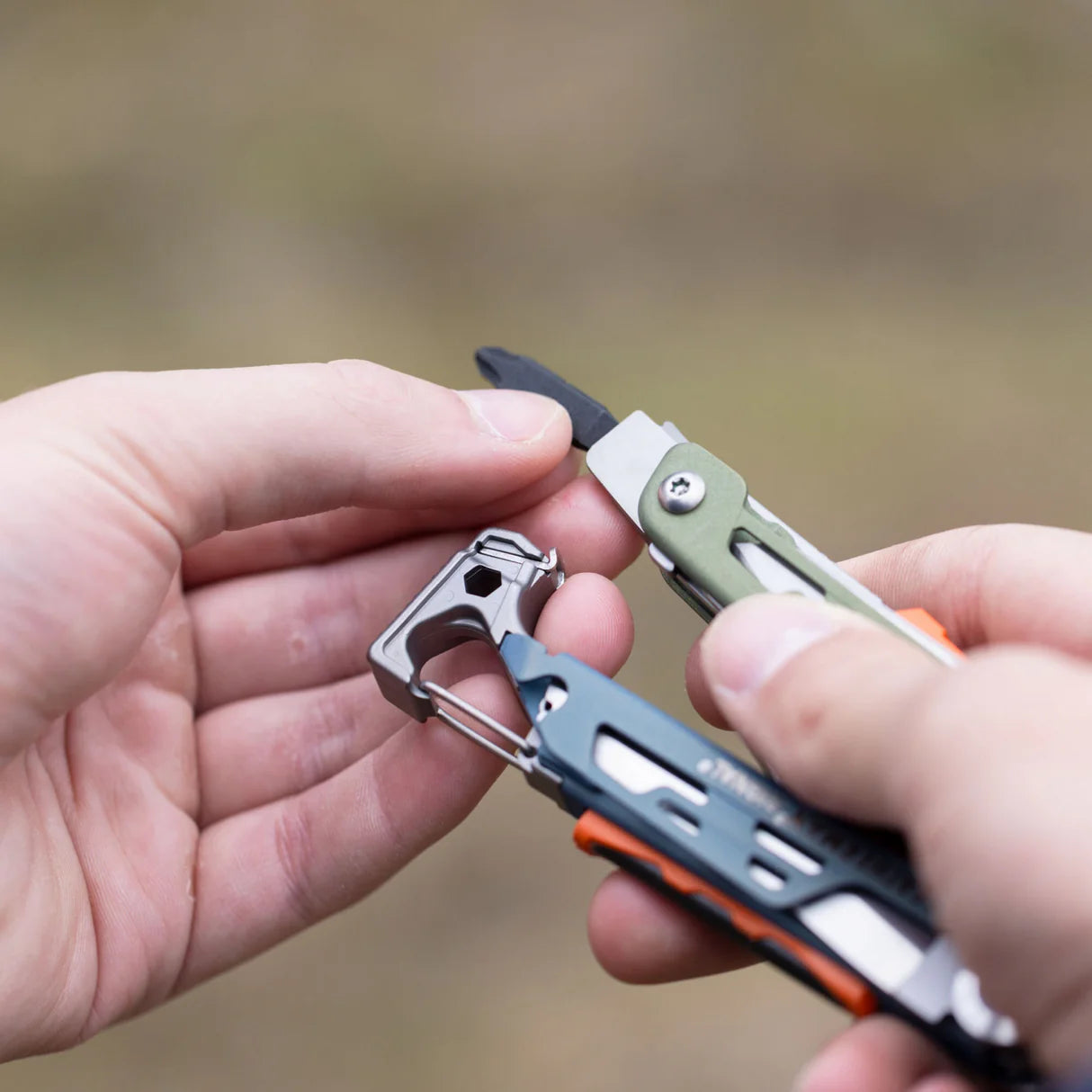 Multitool with various attachments held by hands against a blurred natural background