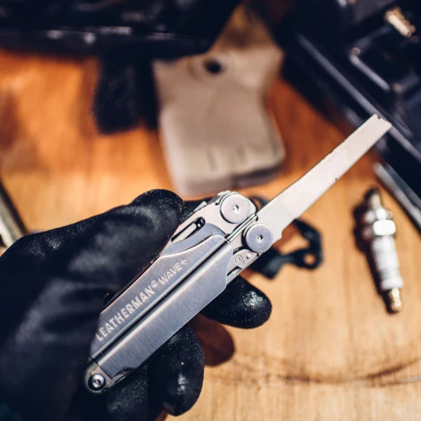 Leatherman Wave multitool held by a gloved hand on a wooden surface with tools in the background