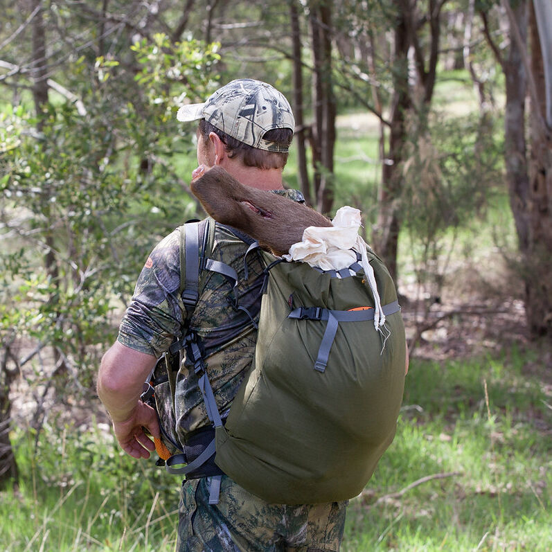 Person in camouflage clothing with a green backpack in a forest setting