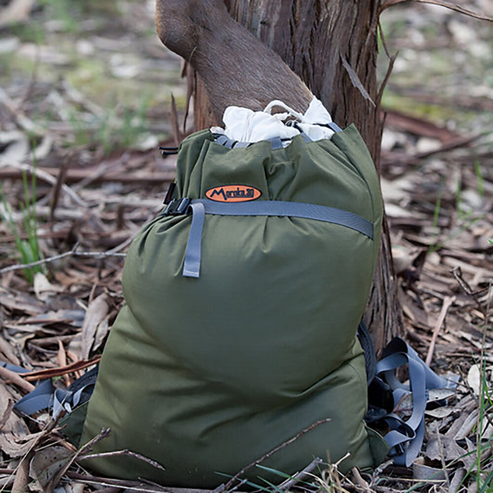 Green backpack with a deer leg on a tree trunk in a natural setting