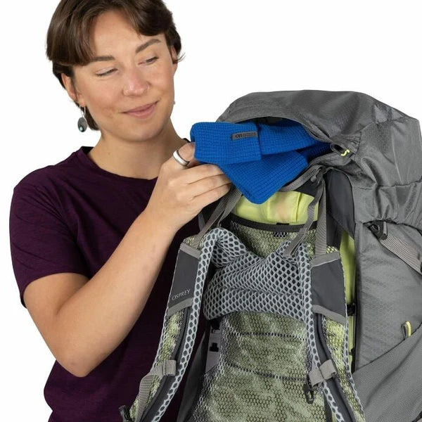Person organizing items in a large gray backpack with a white background
