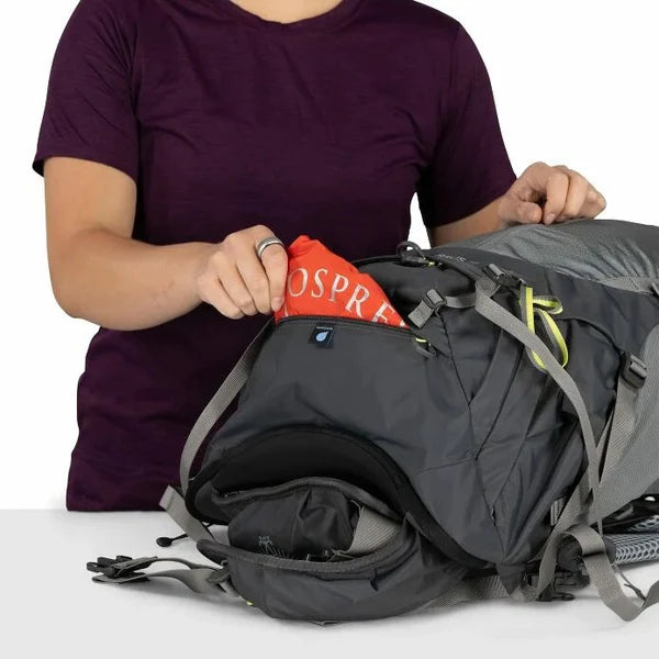 Person packing a backpack with a visible Osprey logo on a white background