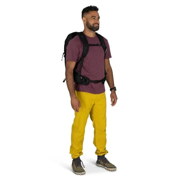 Man wearing a purple shirt, yellow pants, and a black backpack on a white background