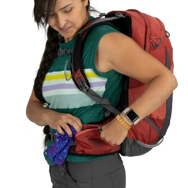 Woman with a red backpack adjusting something inside it on a white background