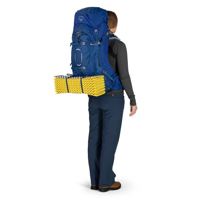 Woman wearing a large Osprey blue backpack with yellow sleeping mat on a white background