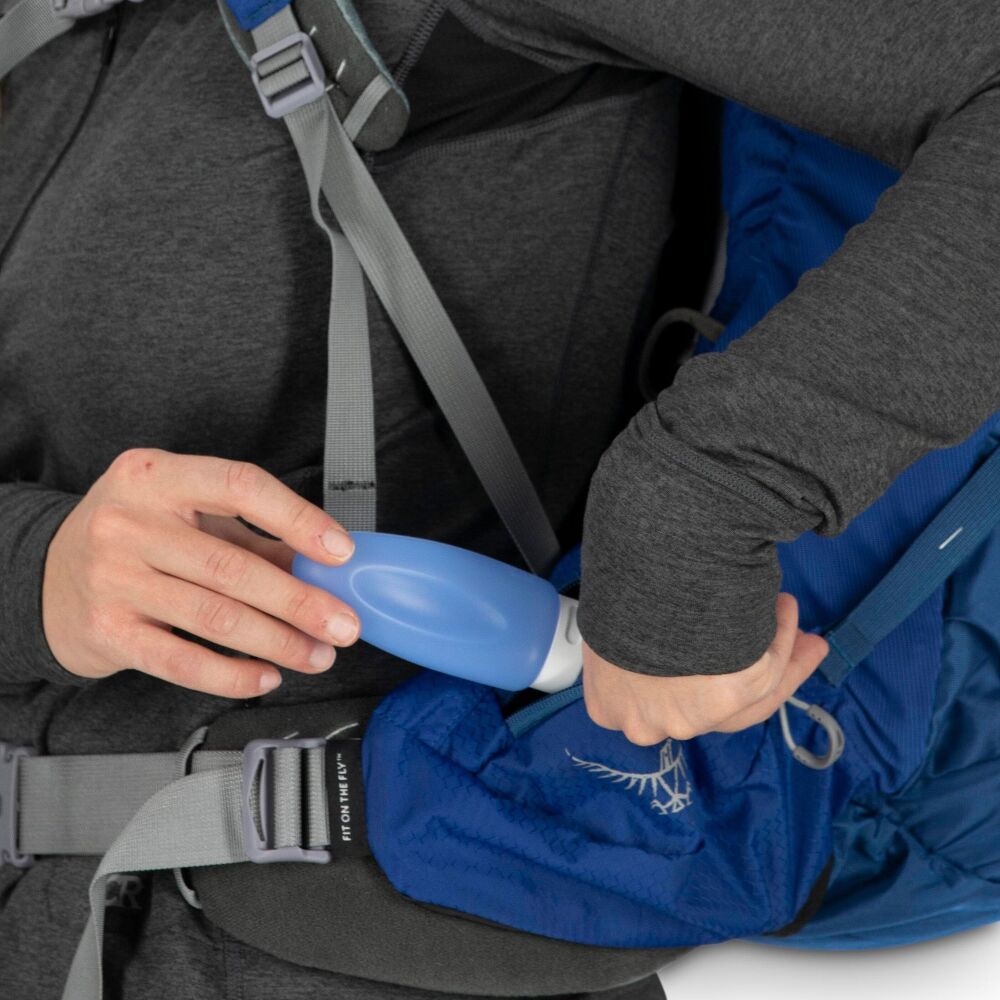 Person adjusting a blue water bottle inside a backpack with visible Osprey logo.