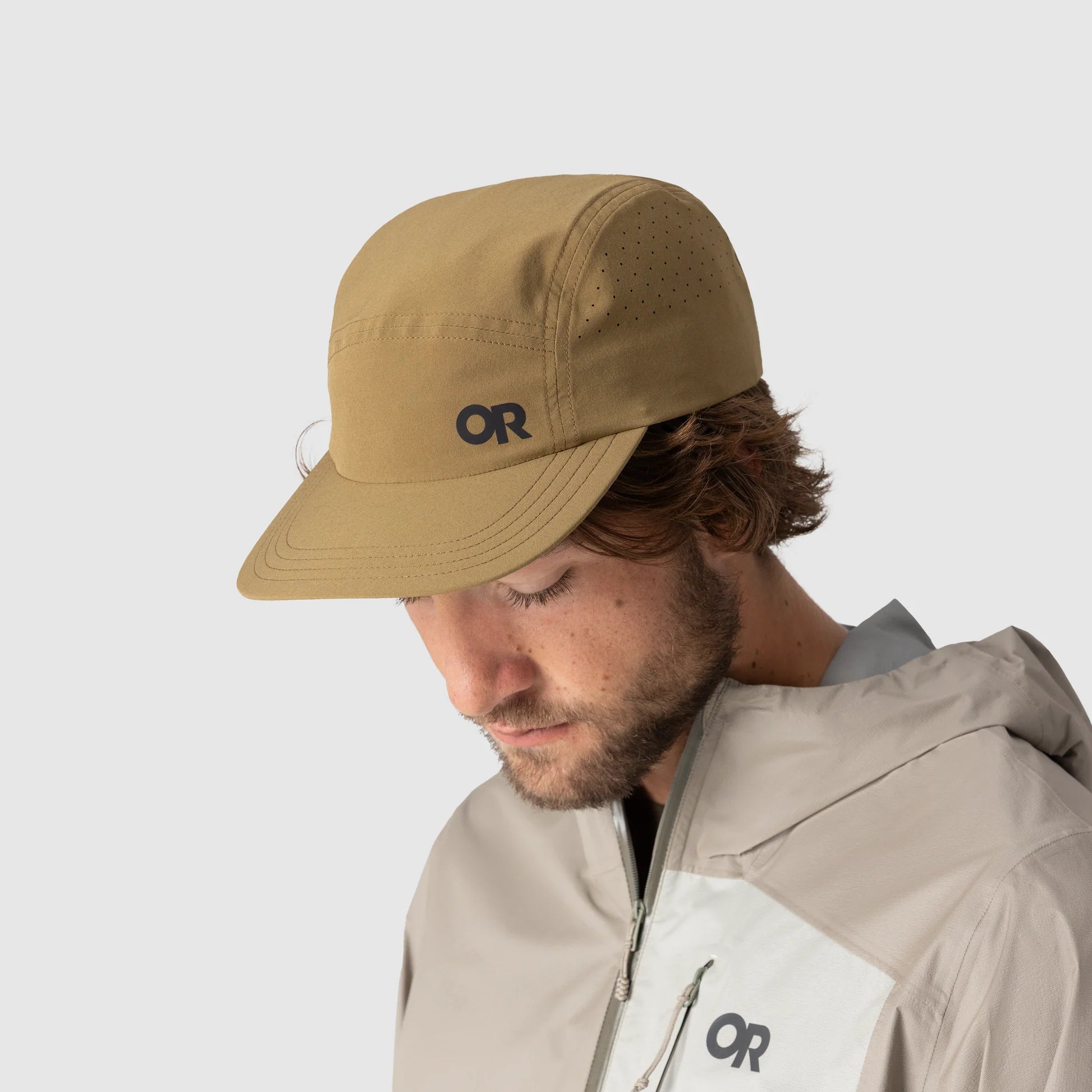 Mens wearing an outdoor research tan cap and jacket with a brand logo on a light gray background