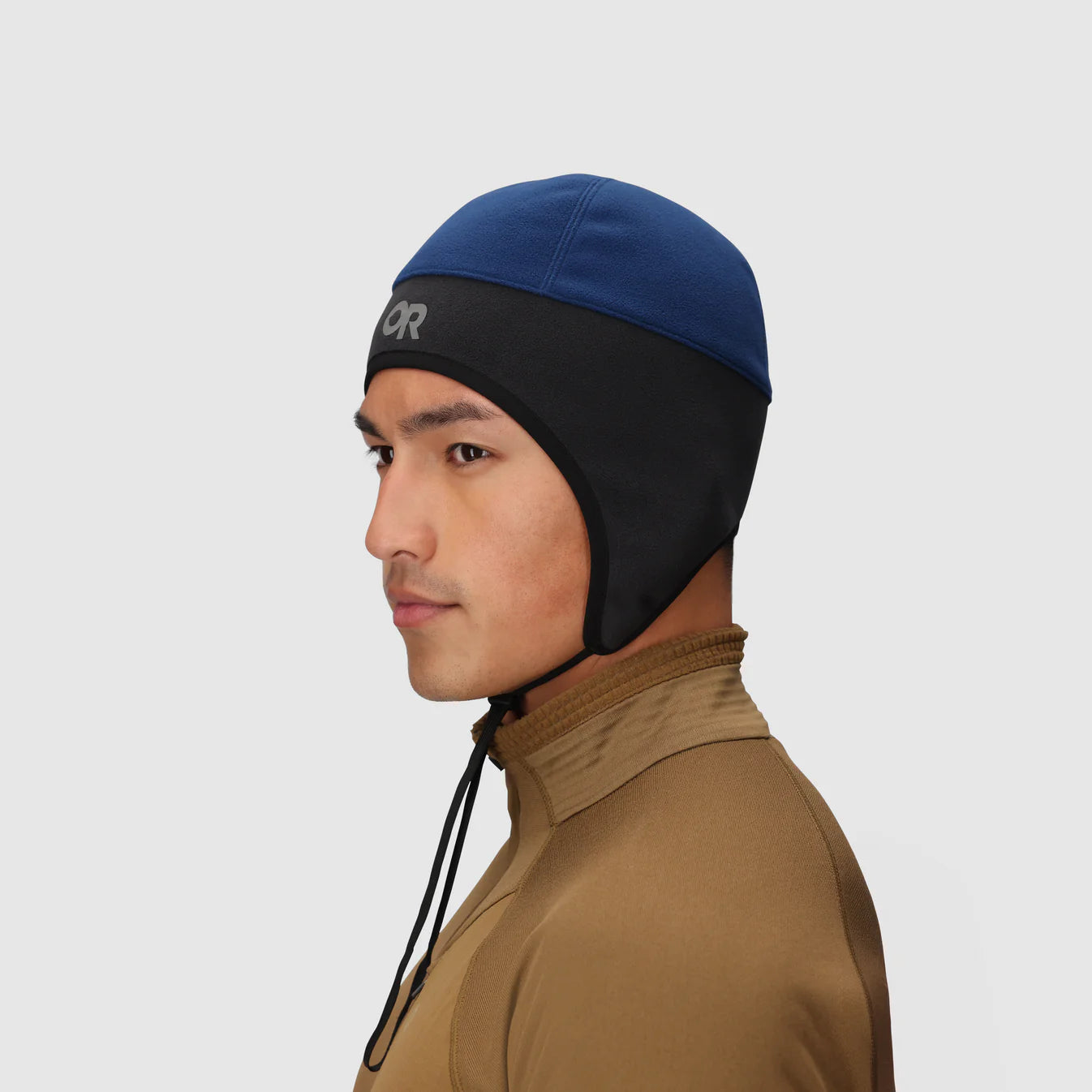 Man wearing a blue and black beanie with a brand logo on a light gray background
