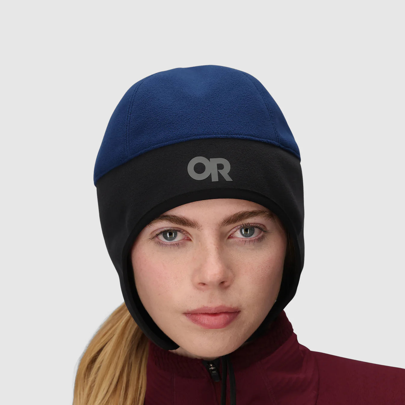 Woman wearing a blue and black beanie with a brand logo on a light gray background