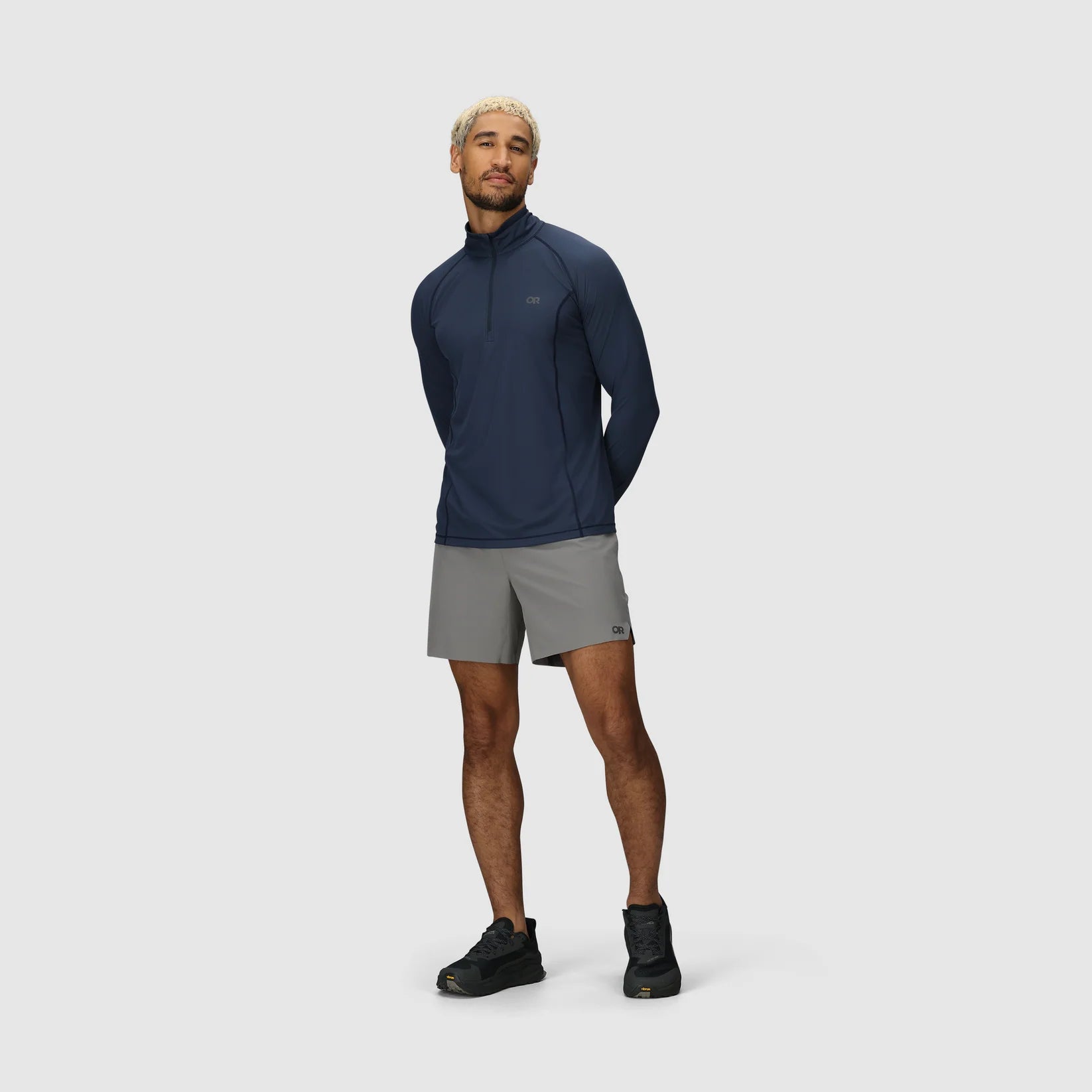 Man wearing a navy blue hiking jacket and gray hiking shorts on a white background