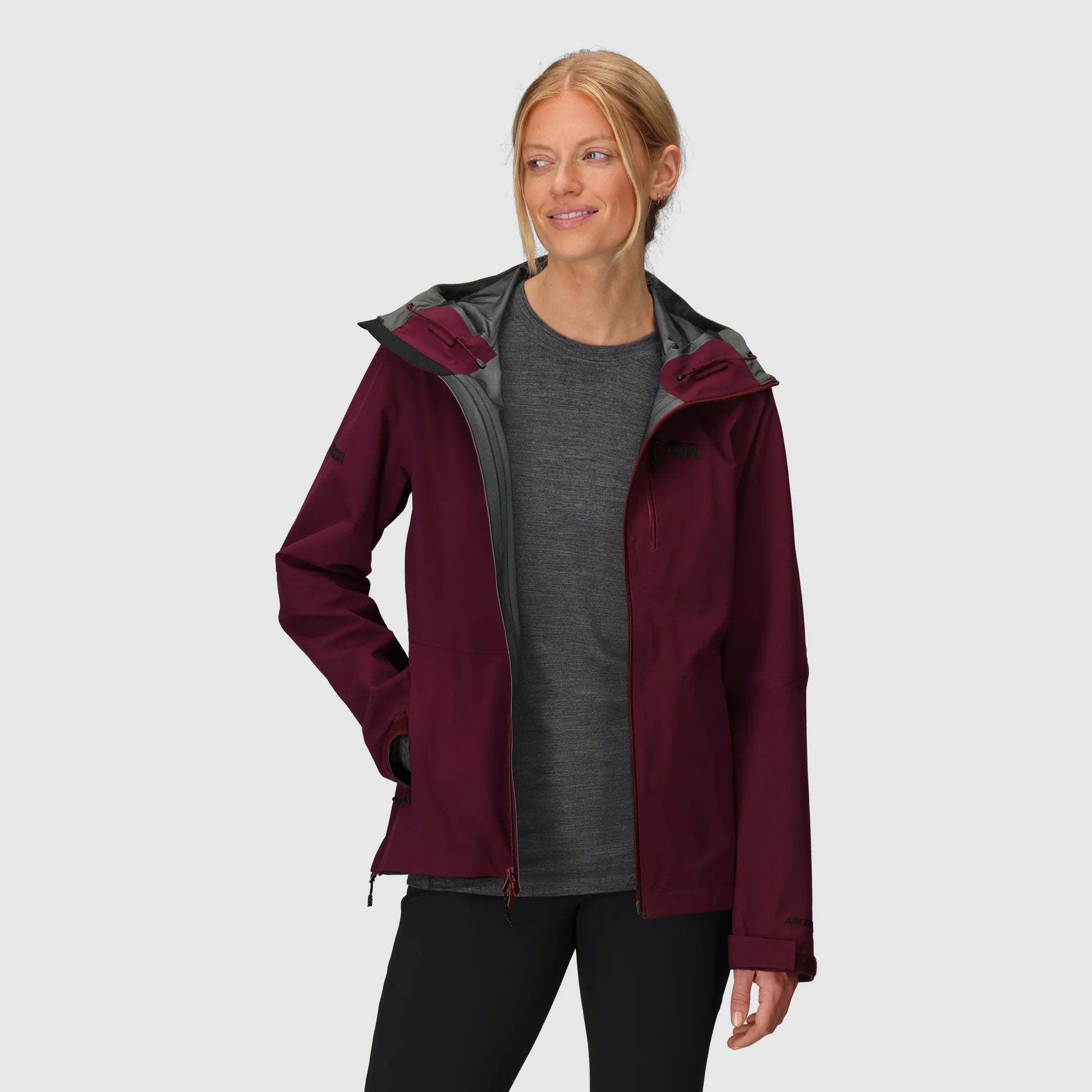 Woman wearing a maroon Outdoor Research Hiking Jacket with a gray hood on a white background