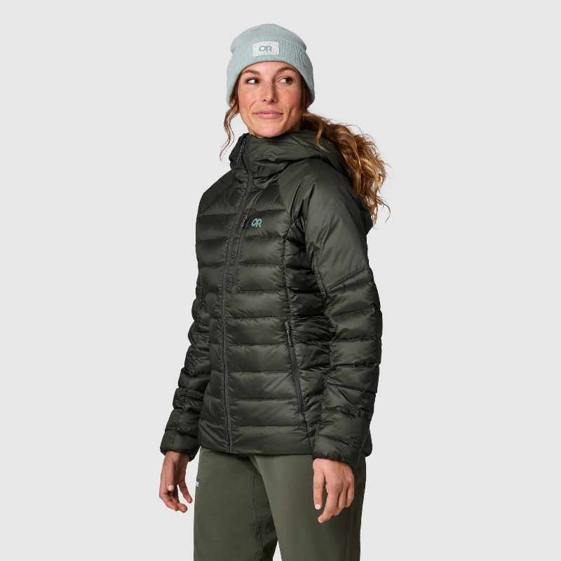 Woman wearing a dark green puffer jacket and light gray beanie on a white background