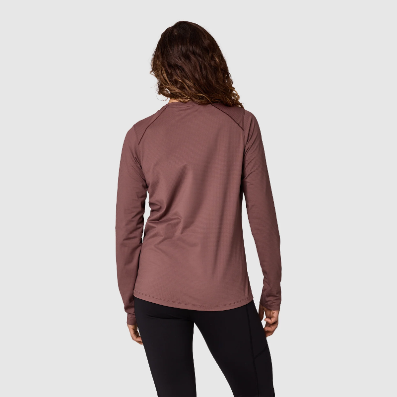 A woman shown from the back wearing a long-sleeve athletic top in a dusty rose color, paired with black leggings, against a light gray studio background.