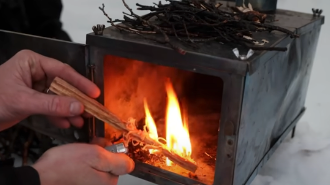 Person lighting a fire in a small stove with flames visible