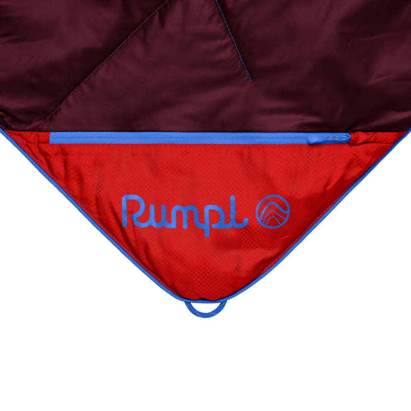 Close-up of a camping sleeping bag or tent showing the red interior with blue piping and the blue embroidered Pumpl logo, against a white background.