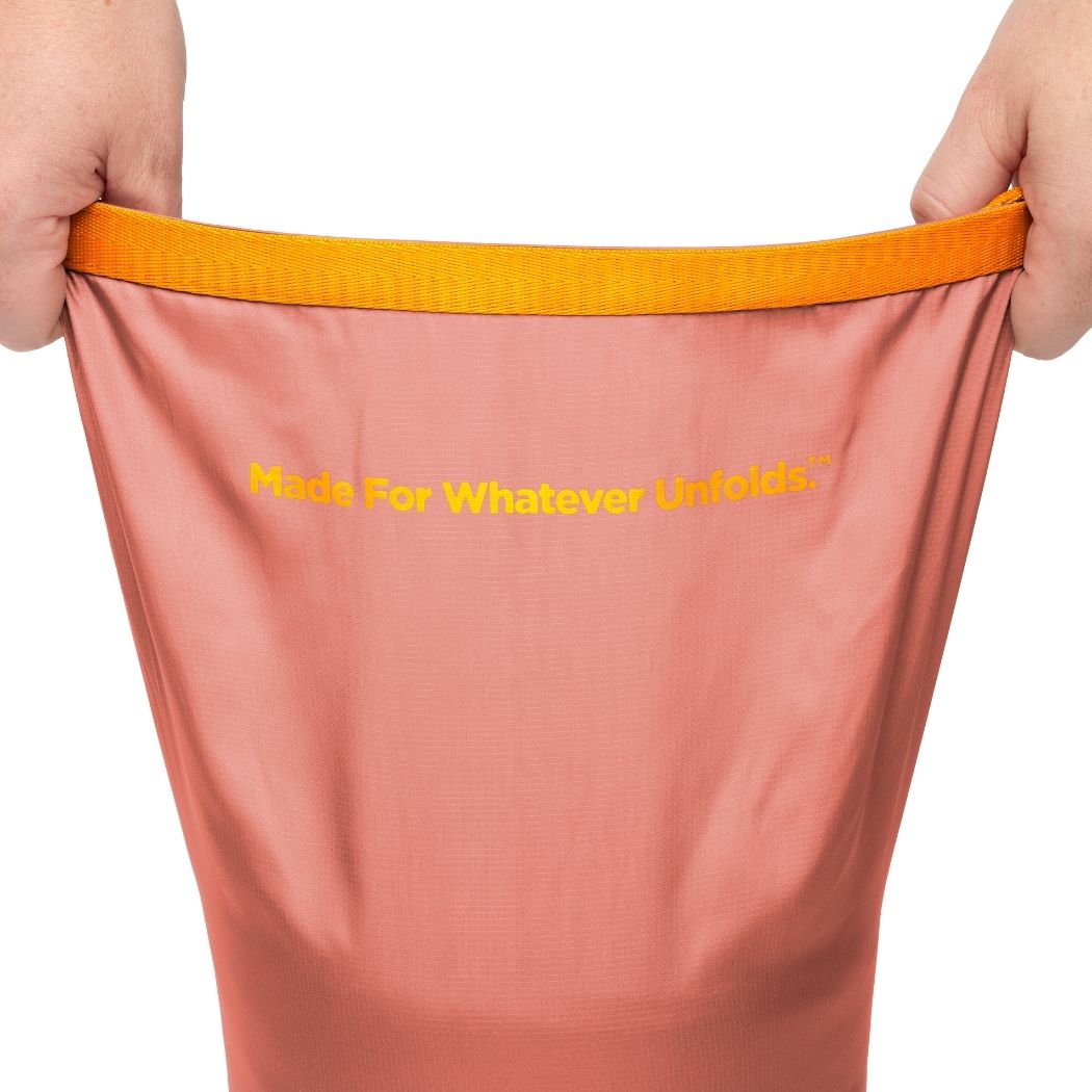 Pink pants with orange waistband held open by hands, featuring the text 'Made For Whatever Unfolds' on a white background.