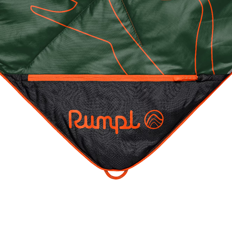 Close-up of a camping sleeping bag or tent showing a dark green outer fabric with orange piping and a black inner panel printed with the orange Rumpl logo.