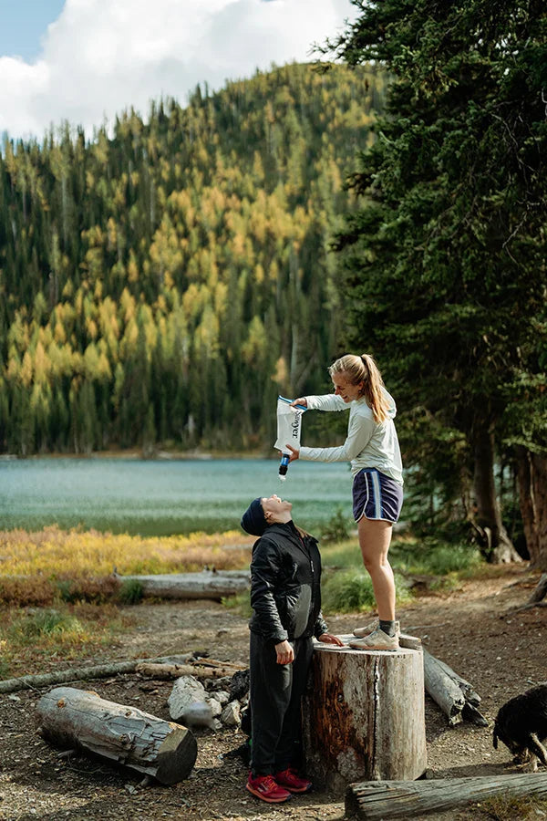 Sawyer Squeeze Water Filtration System w/ Cnoc Premium 2L Bladder squeezing water into someones mouth