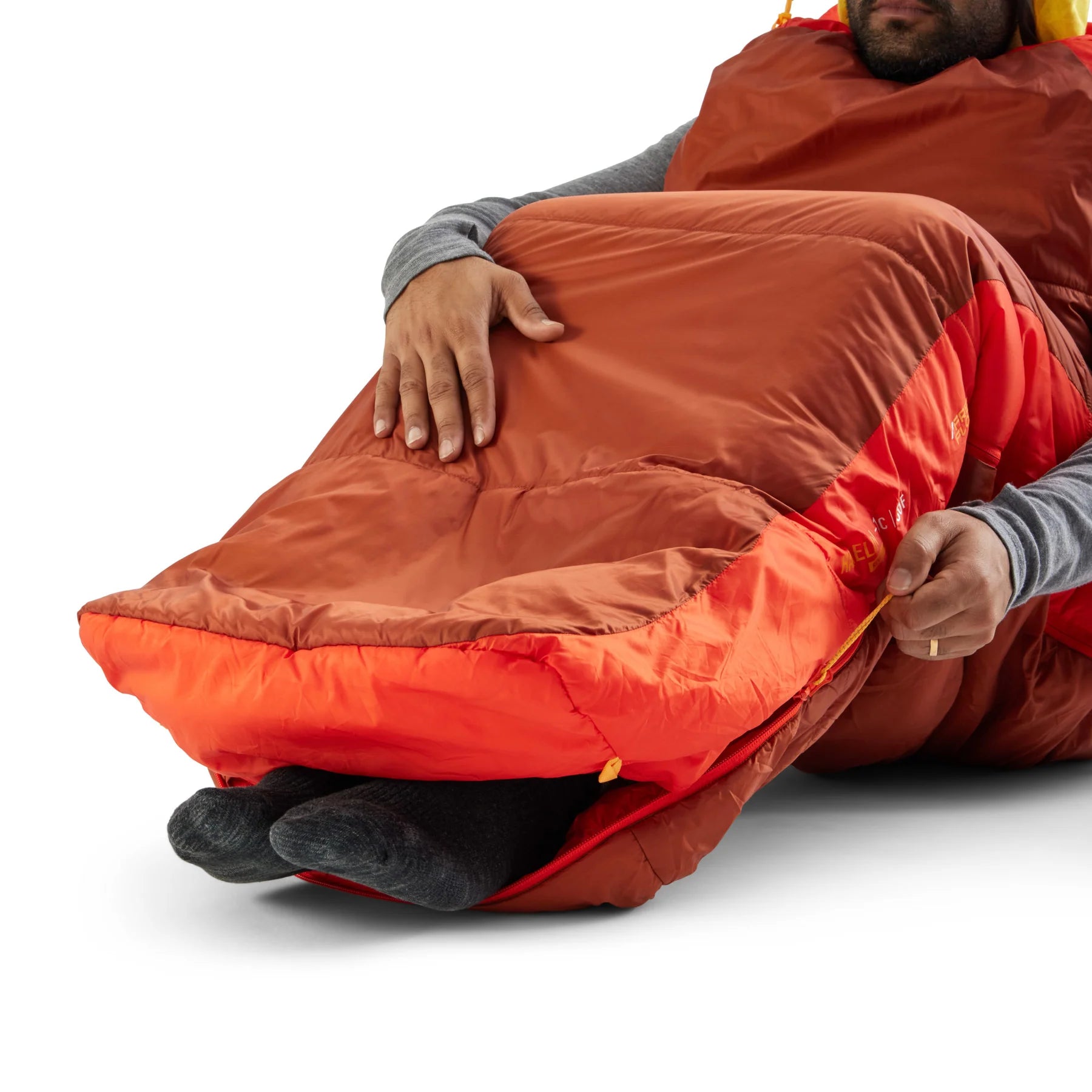 Person lying in a red and orange sleeping bag on a white background