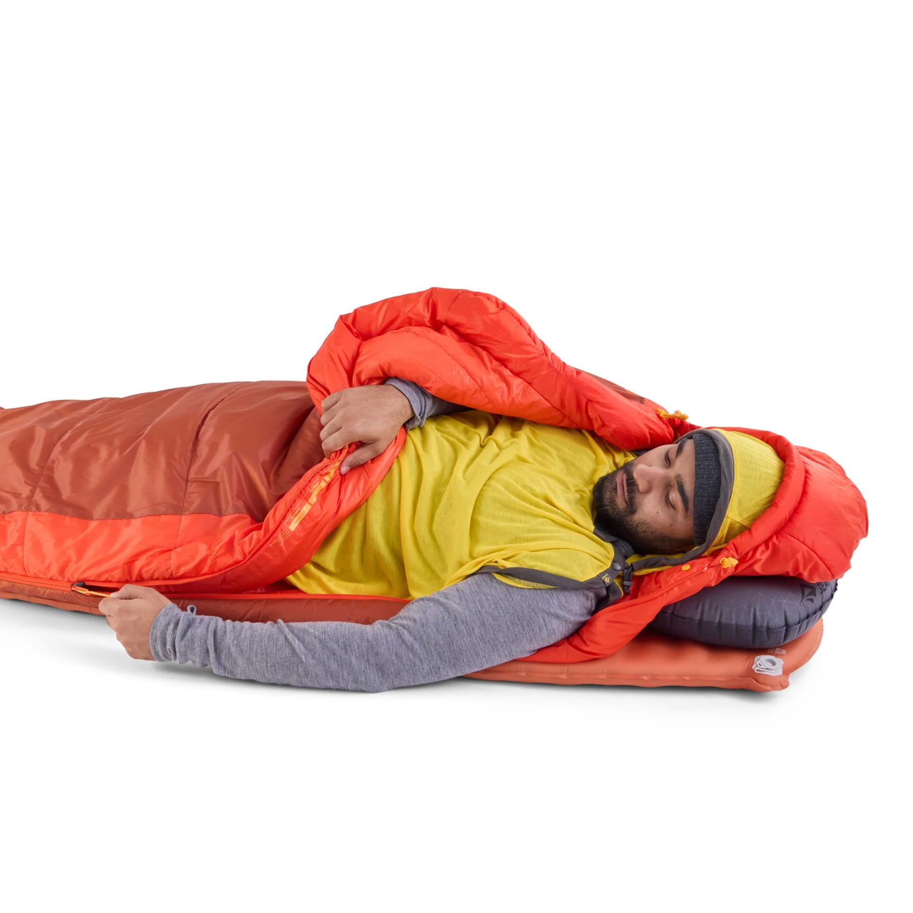 Person lying in a red and orange sleeping bag on a white background with a liner