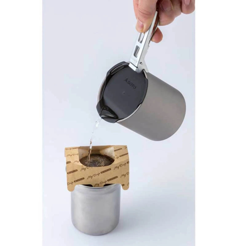 Person pouring liquid from a metal cup into a tea bag holder on a white background