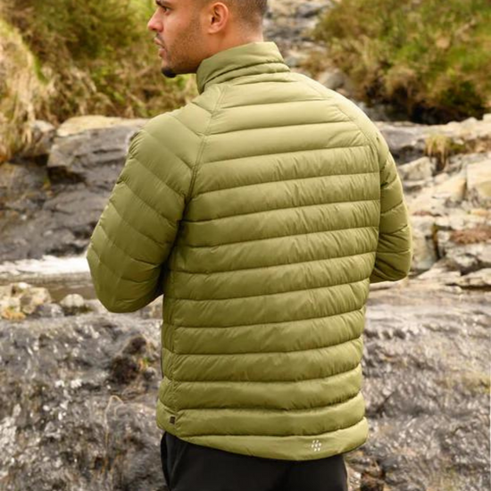 Man wearing a green puffer jacket standing by a rocky stream.