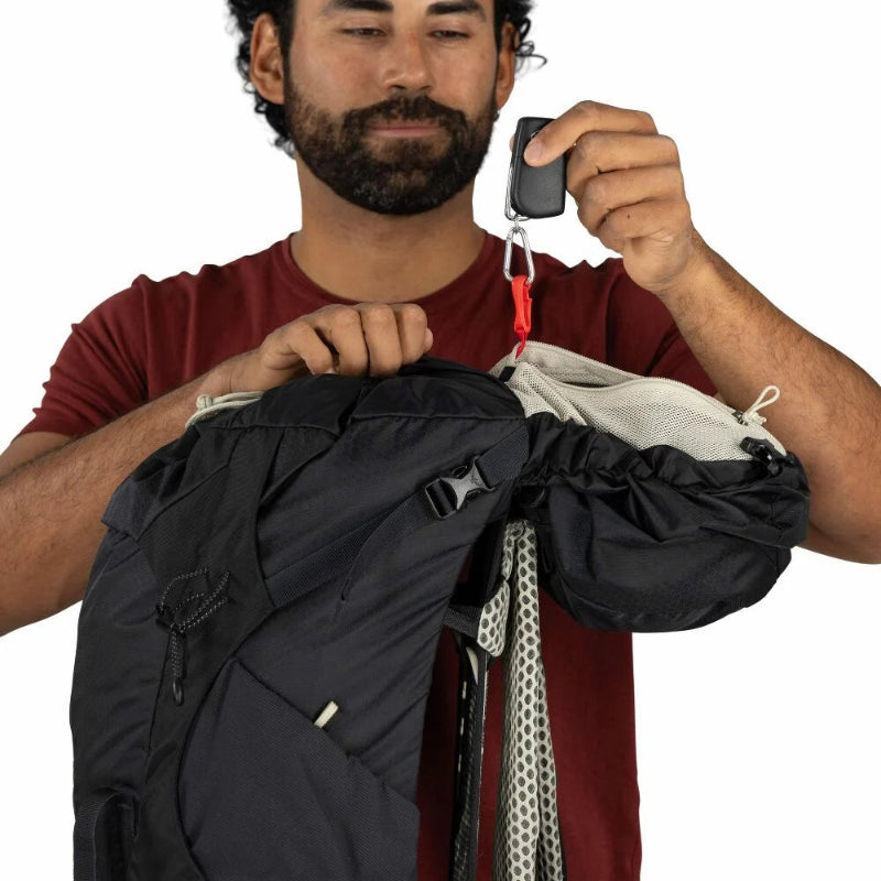 Man measuring a backpack with a digital weight scale against a white background