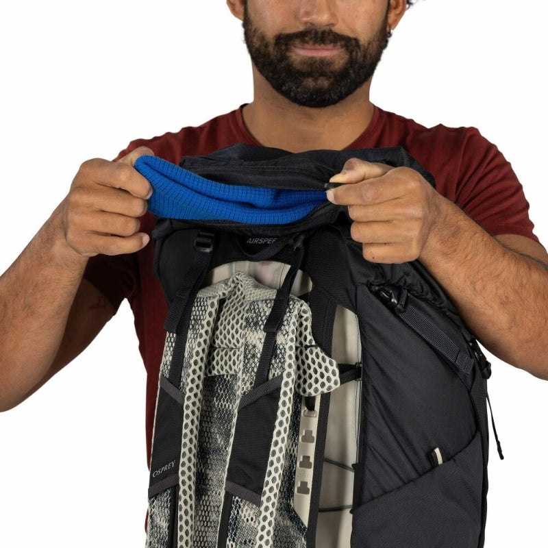 Man holding a black backpack with a blue mesh pocket on a white background