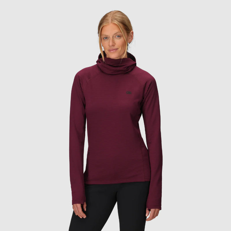 Woman wearing a maroon long-sleeve top with a high collar on a light gray background