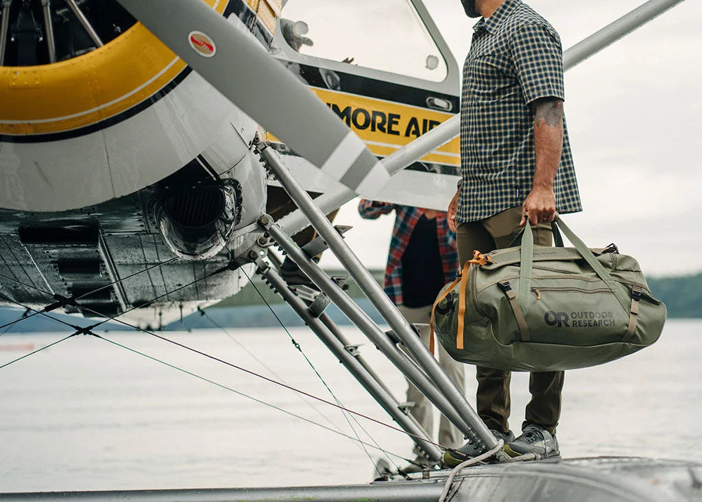 Man with a duffel bag boarding a small airplane on a cloudy day.