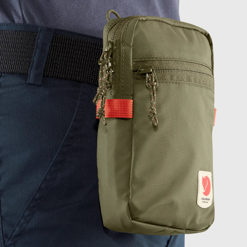 Green pouch with a brand logo attached to a person's pants on a light gray background