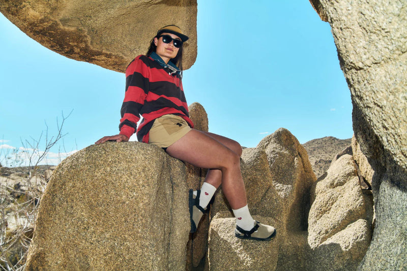 Person sitting on a rock in a desert landscape wearing a red and black striped shirt.